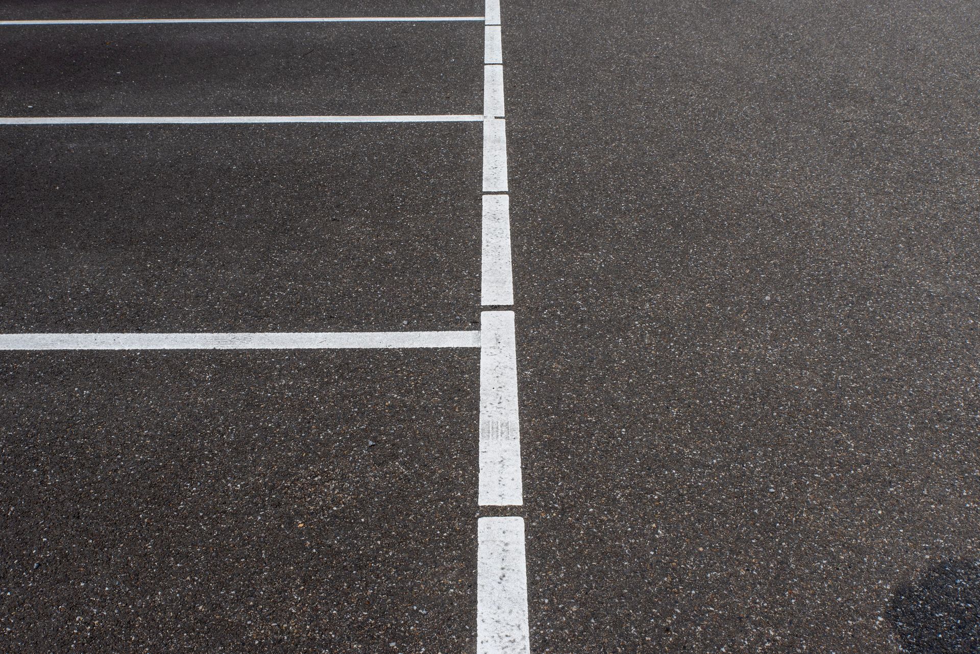 Asphalt parking lot showing white lines marking parking spaces. Minimalist urban scene.