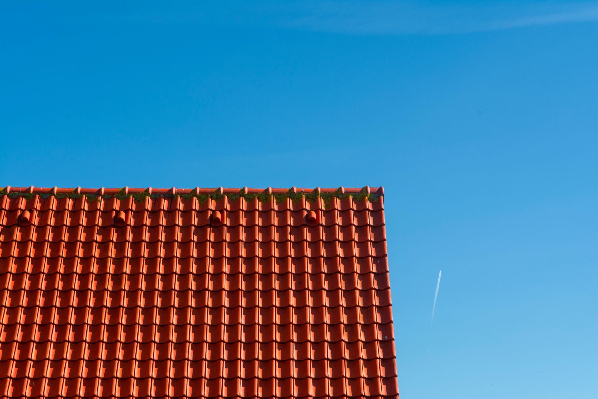 Minimalist photo of a red tiled rooftop contrasting against a clear blue sky.